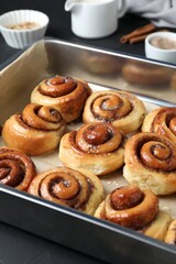 Baking dish with tasty cinnamon rolls on dark table
