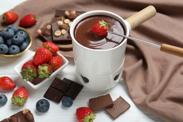 Dipping fresh strawberry in fondue pot with melted chocolate at white wooden table