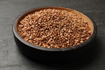 Bowl with dry buckwheat on black table, closeup