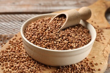 Bowl and scoop with dry buckwheat on wooden table, closeup