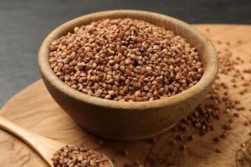 Bowl and spoon with dry buckwheat on table, closeup