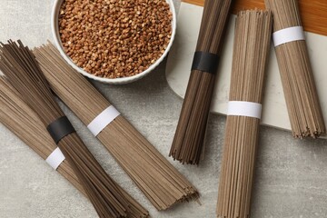 Uncooked buckwheat noodles (soba) and grains on light grey table, flat lay