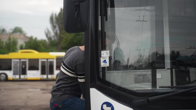 Professional driver comes up to trolleybus and opens door to enter it. Young man in casual clothes heading to blue electric vehicle to start working day