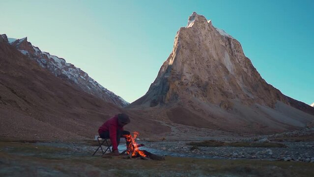 Indian man making bonfire in front of the Gonbo Rangjon mountain at Zanskar in Ladakh, India. Tourist lights bonfire to keep himself warm during the cold weather in the Himalayas. Adventure background