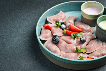 Dumplings with strawberries and sour cream. On a black stone background. In a plate, close-up.