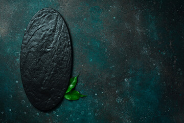 Oval slate black plate. On a dark green-turquoise background. Free space for text.