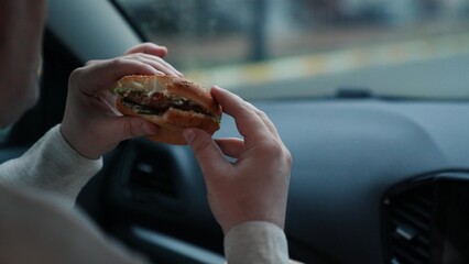 Hungry woman bites piece of burger satisfying hunger and sitting in vehicle - obrazy, fototapety, plakaty