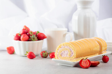 Delicious biscuit roll cake with fresh strawberries on a white stone table.