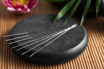 Acupuncture needles and spa stone on bamboo mat, closeup