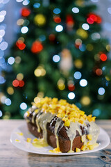 Fototapeta na wymiar Christmas stollen stands on a plate on a wooden table against the backdrop of a sparkling Christmas tree
