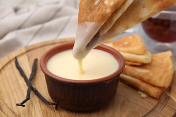 Dipping crepe into tasty condensed milk at table, closeup