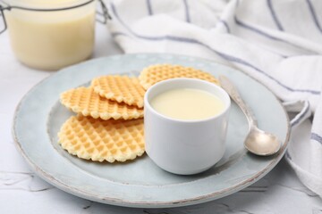 Tasty condensed milk and waffles on white textured table, closeup