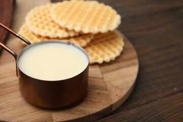 Tasty condensed milk and waffles on wooden table, closeup. Space for text