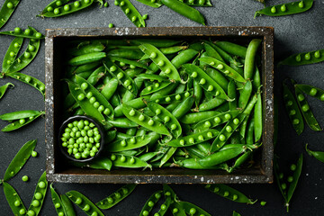 Pods of green peas with leaves in a wooden box. On a black stone background. Top view. Healthy food. - obrazy, fototapety, plakaty