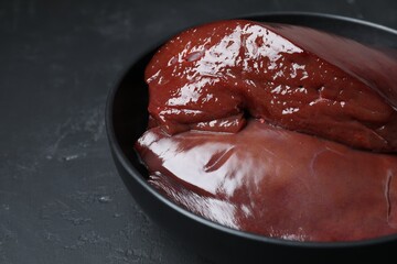 Pieces of raw beef liver in bowl on black table, closeup