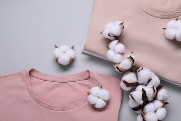 Cotton branch with fluffy flowers and t-shirts on light gray background, flat lay