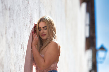 Naklejka premium Young, beautiful blonde woman with blue eyes is leaning against the wall and dressed in casual, modern clothes. The woman makes different expressions with her face, smiling, serious, happy and sad.
