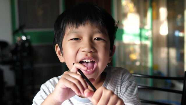 Asian kid child boy with pencil on ear sing song with relax face to build power before doing school exercise homework at home. Concept of funny shot, relaxation, education, home school.