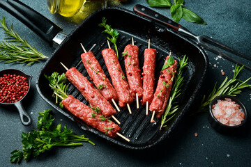 Lula kebab on skewers with spices and herbs in a pan. On a dark stone background. Top view.