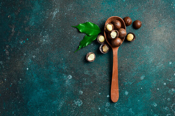 Shelled macadamia nut and peeled macadamia nut on a black textural background in a wooden spoon. Tope view. - obrazy, fototapety, plakaty