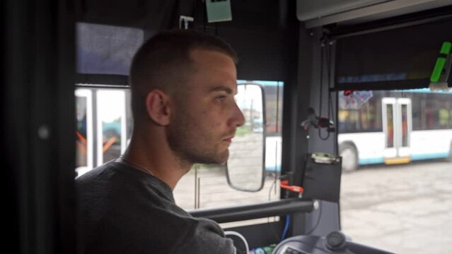 Close up side shot of professional transport operator focused on driving trolleybus along road. Young man in casual clothes concentrated on operating trolley