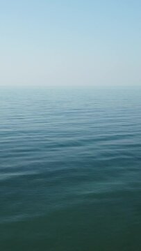 Abstract aerial calm sea summer ocean sunset nature. Small waves on water surface with clear blue sky. Holiday, vacation and recreational concept. Weather and Climate Change. Nobody. Vertical video