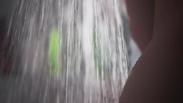 Naked woman washes under flow of water in shower. Bare woman stands enjoying refreshing shower. Nude woman stands under cascade of water in shower