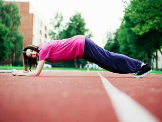 Slim teenager girl doing stretching on a red running line. Selective focus. Sport and fitness concept. Young athlete in red t shirt. Flexibility work out for mobility.