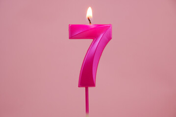 Pink birthday candle burning on pink background. Number 7.