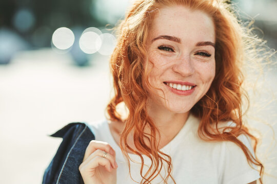 Beautiful red-haired girl having fun on the street. The girls have a beautiful figure, a white T-shirt and jeans with sunglasses
