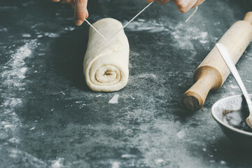 Chef cutting the cinnamon rolls into equal parts thread. Production of cinnamon rolls or Cinnabon on a concrete background. Holiday baking