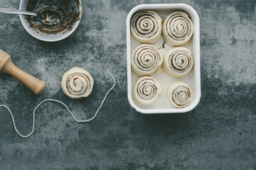 Cooking cinnamon rolls buns on a concrete background. Cinnabons. Raw rolls in a baking dish. top...
