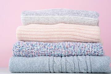 Close up of a stack of winter knitted sweaters on a pink background. Change of season. Conscious consumption. Environmental friendliness and sustainable fashion. 