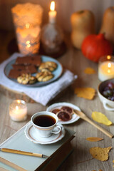 Cup of tea or coffee, plate with desserts, dried oranges, bowl of grapes, scented candles, vintage books, pumpkins and autumn leaves on the table. Autumnal hygge. Selective focus.