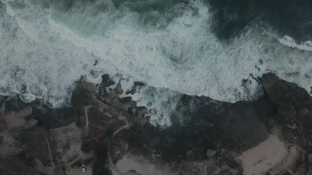 Waves crash white foaming onto the rocks of the Indonesian coast near Baron Beach.