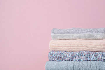 Stack of winter knitted sweaters on a pink background. Change of season. Conscious consumption....