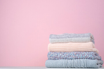 Fototapeta na wymiar Stack of winter knitted sweaters on a pink background. Change of season. Conscious consumption. Environmental friendliness and sustainable fashion. space for text.