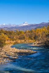 Beautiful autumn landscape mountain river, yellowed trees, mountains with snowy peaks. Charming mountain landscape in autumn. Vertical photo