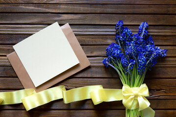 Bouquet of blue grape mouse hyacinths and envelope with blank card with ribbon over wooden background. Blank greeting card mockup. Flat lay, top view. Lovers or happy birthday