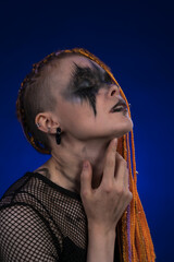 Headshot of young woman with eyes closed, orange color braids hairdo and spooky black stage make up...