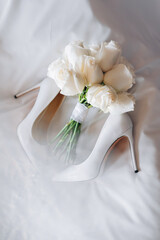 Wedding shoes and bouquet of white peonies on the bed