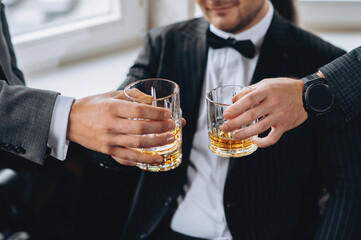 Cropped shot of groom and his friends wear suits holding glasses of whiskey