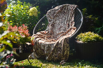 A wicker chair with a blanket stands in the garden.
