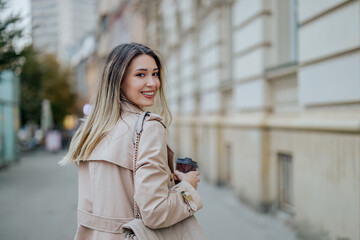 Fototapeta premium Woman walking while looking over her shoulder and drinking coffee takeaway