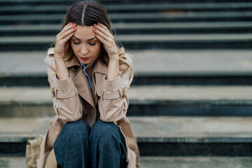 Fototapeta premium Depressed and sad woman sitting on a stairs and holding her hands on her head