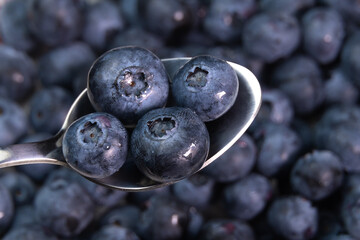 Teaspoon with four blueberries over a whole bowl of ripe blueberries, macro photography, copy...
