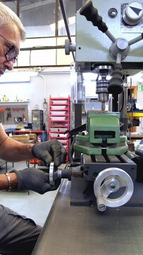 vertical shot of a brass musical instrument repairer using a vertical drill to restore the tubing of a French horn in a luthier's shop