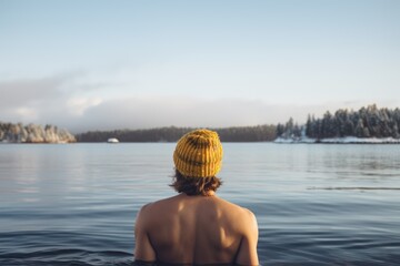 Young man in a hat bathing in the cold water of the lake. Wim Hof method, cold therapy, breathing techniques, winter swimming, ice swimming. - obrazy, fototapety, plakaty