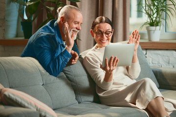 Side view portrait of old lovely couple elderly man and senior woman with tablet while online chatting or on video call with greeting. Technology concept.