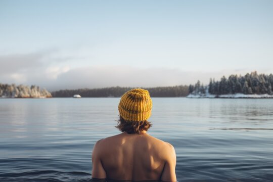 Young man in a hat bathing in the cold water of the lake. Wim Hof method, cold therapy, breathing techniques, winter swimming, ice swimming.